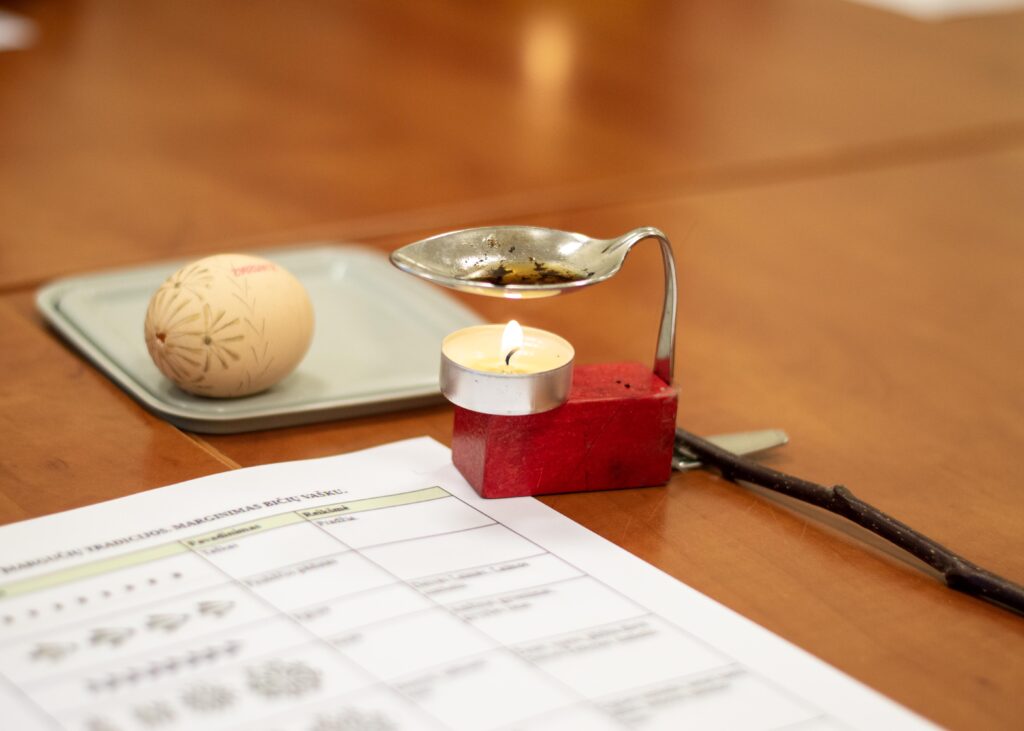 Edukacijos akimirka. Priemonės skirtos kiaušinių marginimui bičių vašku: kiaušinis, raštų pavyzdys, žvakė, stovelis vaškui tirpinti, pagaliukas su adatėle.